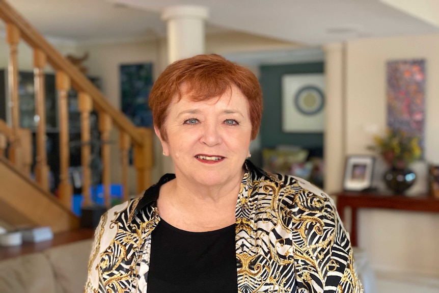 A woman with red hair in her room with a staircase behind her.