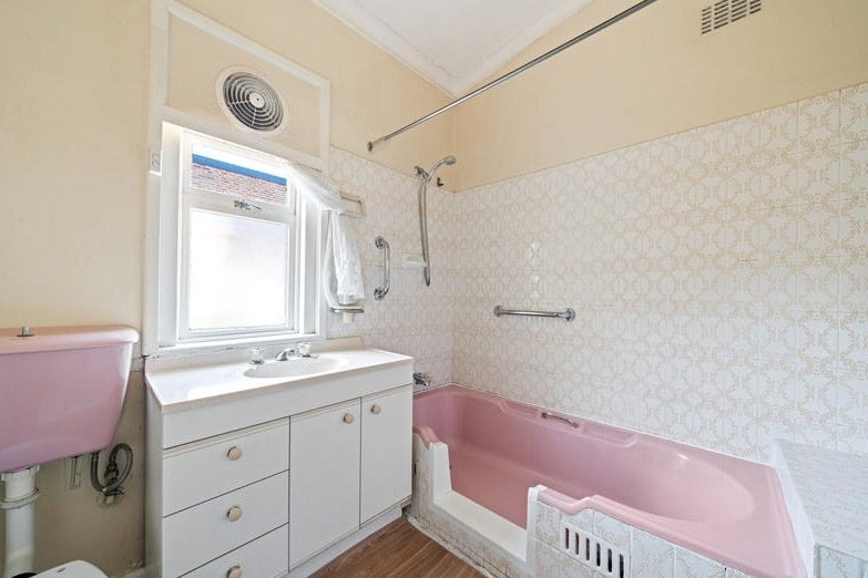 A dated old bathroom with a pink bath