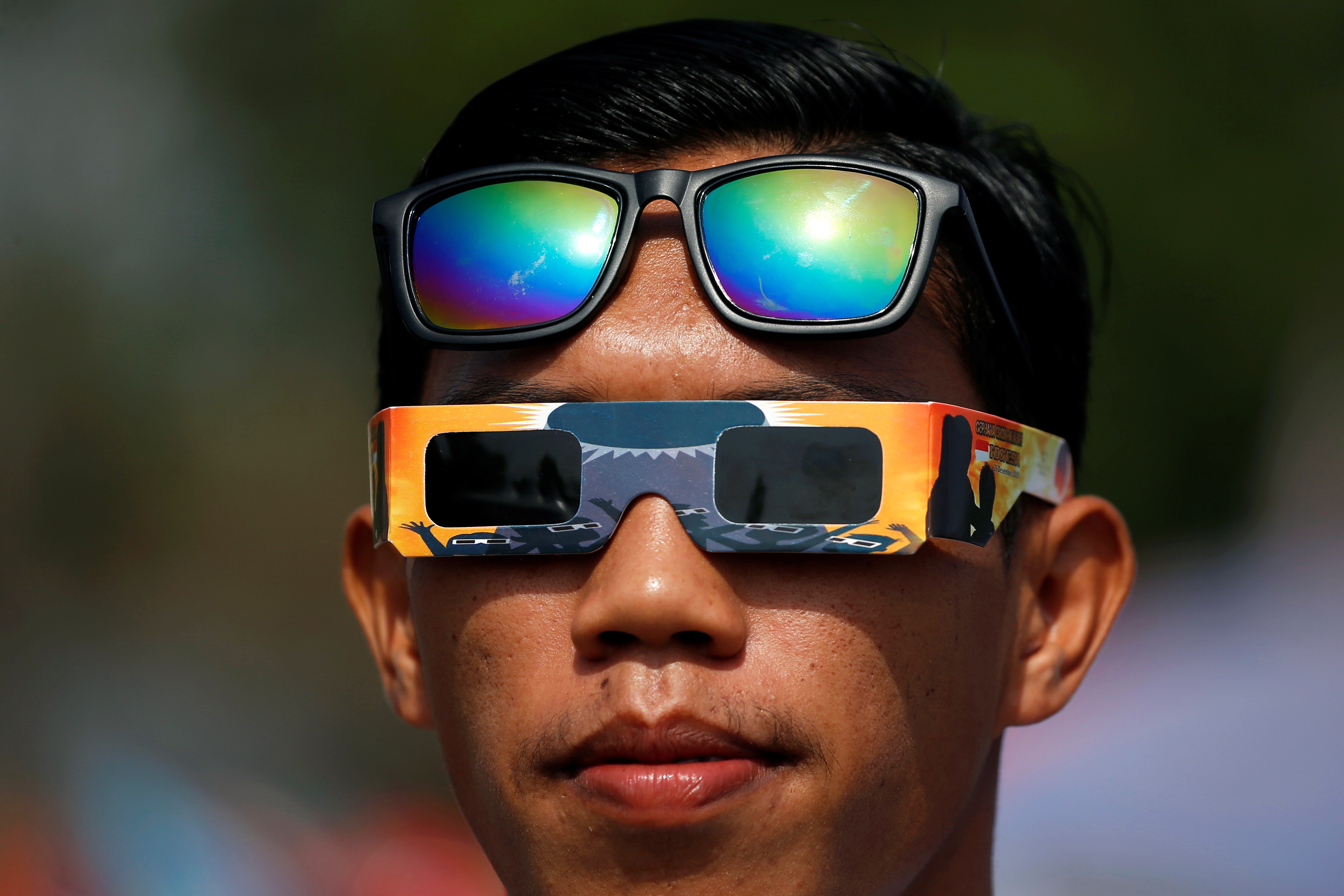 A man wears special solar eclipse glasses on his eyes, with his sunglasses resting up higher on his head. 