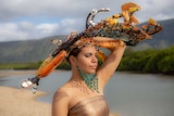 Indigenous model with elaborate headpiece standing in front of an estuary