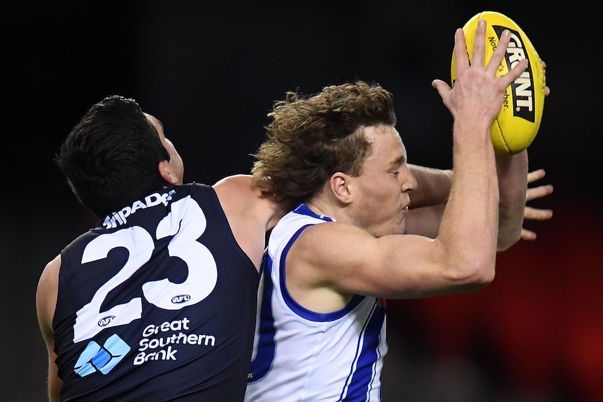 A young man in white jersey marks a yellow ball under pressure from an opponent in black jersey wearing No 23.