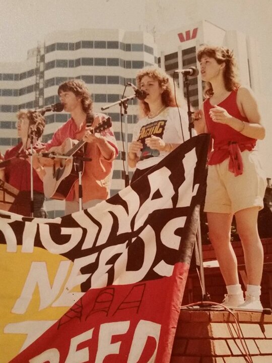 A band performing on stage at an open-air concert in Perth near an Indigenous flag