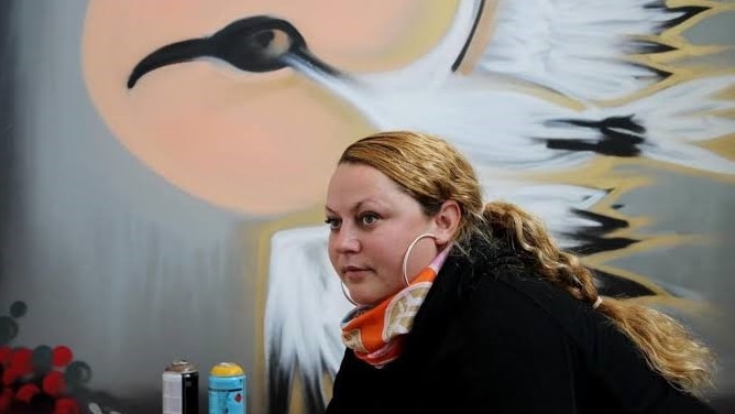 A woman poses for a photo in front of a graffiti crane.