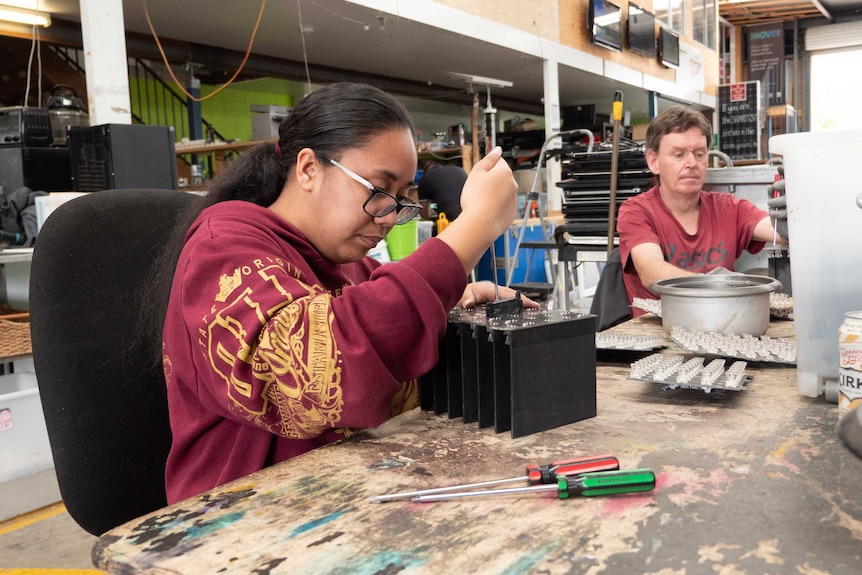 A young woman and a man sitting at a table repairing electronic items.