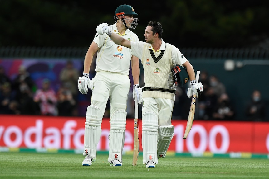 Australia batter Travis Head punches the air while carrying his bat and helmet. Teammate Cameron Green is behind him.