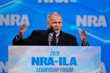 National Rifle Association President Col. Oliver North speaks at a podium in front a of bight blue NRA background