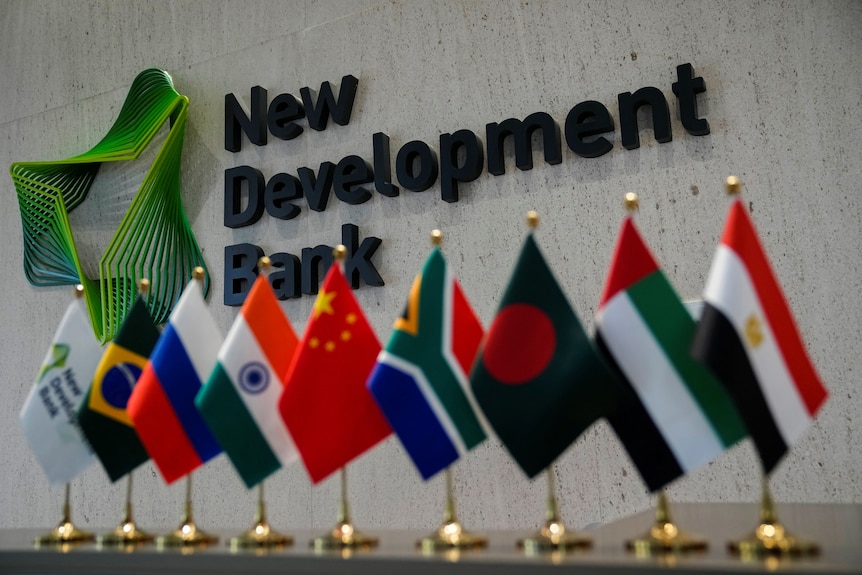 Flags lined up in front of a sign that says "New Development Bank"