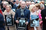 People march in the street carrying large black-and-white photos of their family members with their names and the word 'justice'