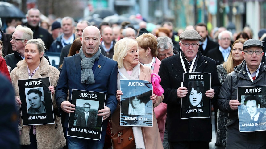 People march in the street carrying large black-and-white photos of their family members with their names and the word 'justice'