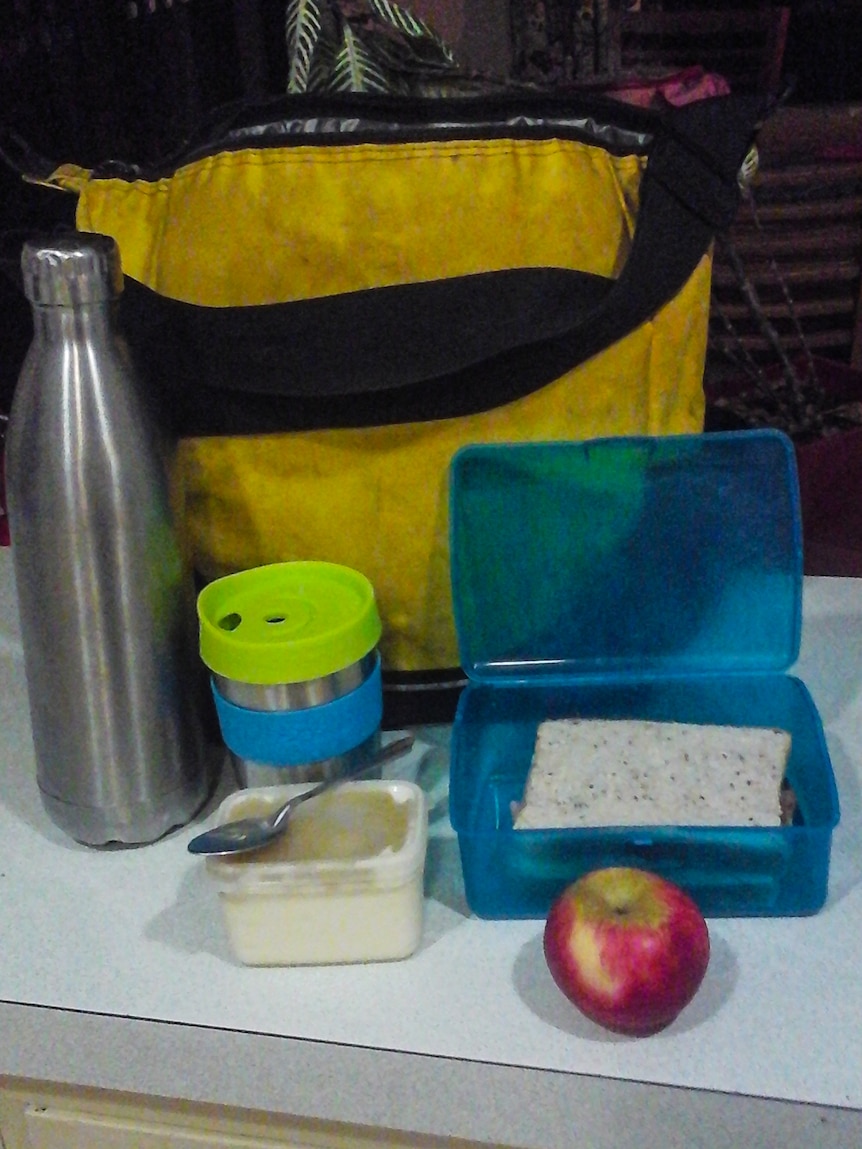 A yellow shoulder bag behind a blue sandwich box, keep cup and metal water bottle