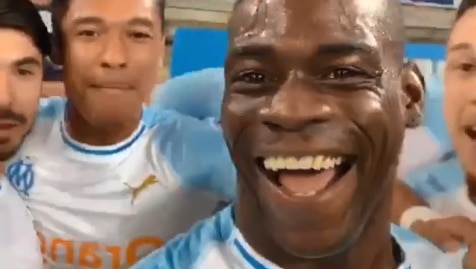 Mario Balotelli smiles at the camera with his teammates behind him and fans in the background