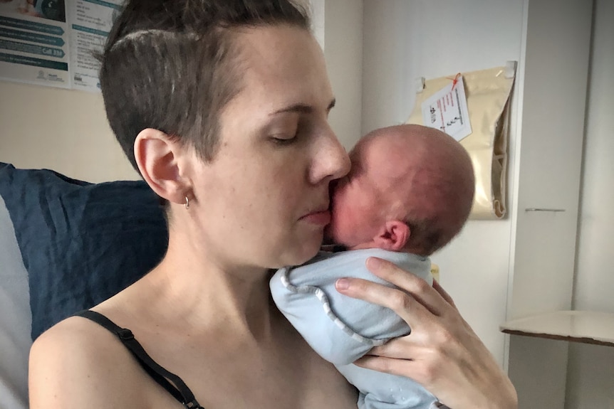 A woman with shaved head holds her a small baby 