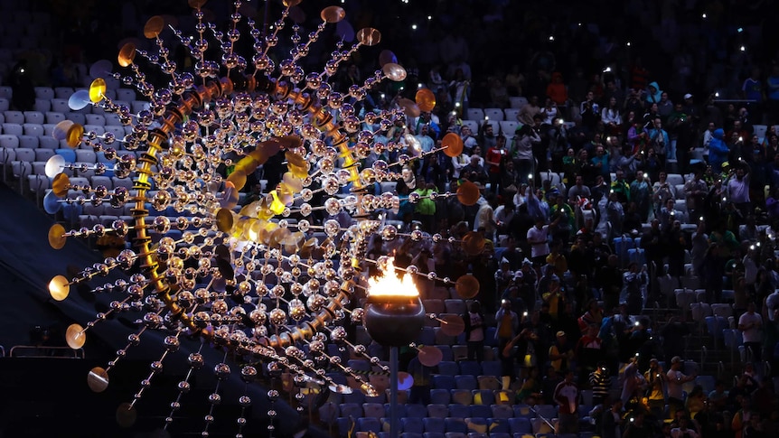 Spectators sit beside the cauldron with the Olympic flame at the Rio Games closing ceremony.