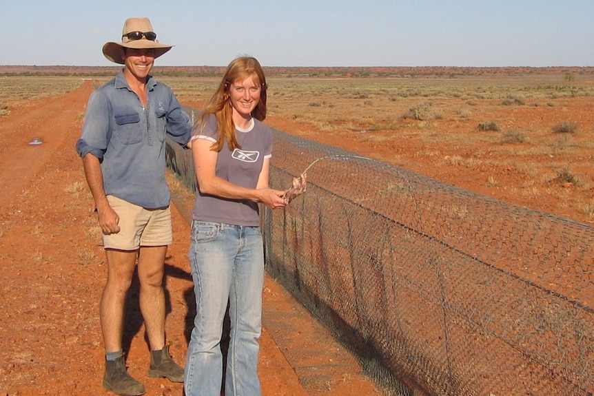 Man and women looking at camera while fixing a wire fence in red desert scene