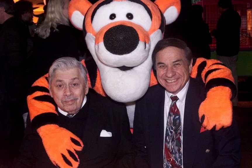 Two men stand with a cartoon mascot of the creature Tigger.