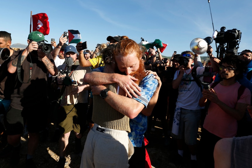 A red haired man hugging a person, surrounded by a crowd of photographers. 