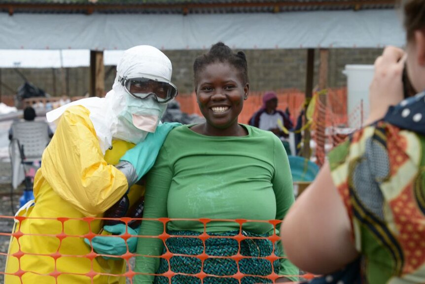 A health worker in a yellow protective suit poses with a woman in an ebola hospital in Liberia