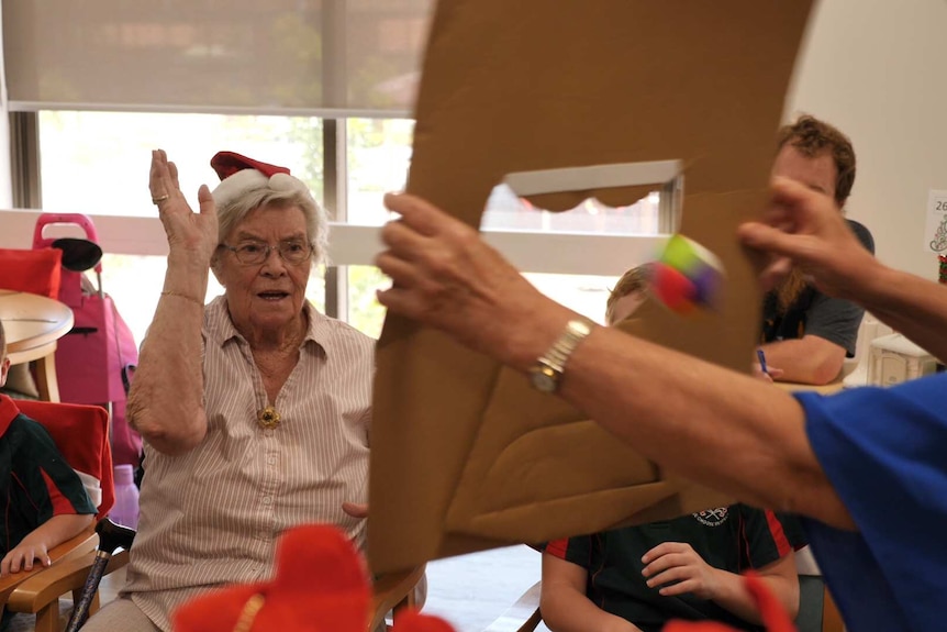 Older woman throws a ball through a cardboard Santa face.