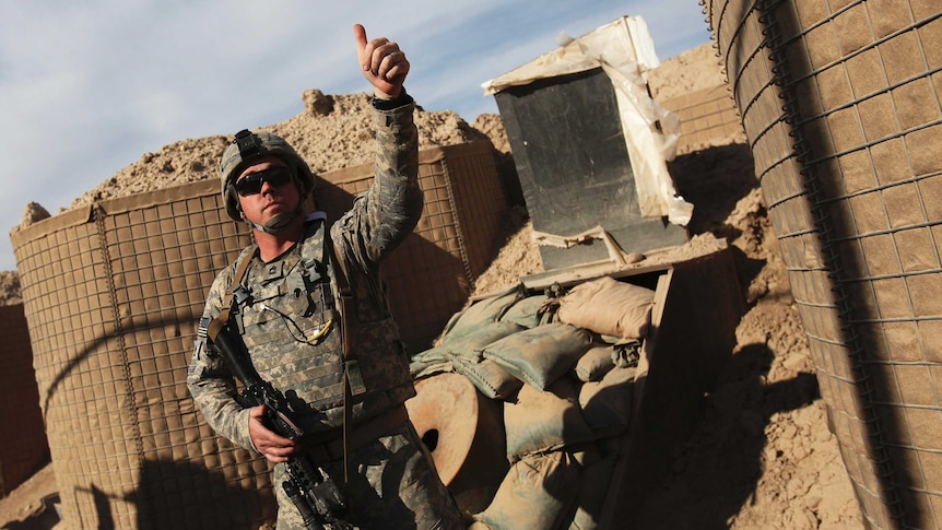 A US soldier gives a thumbs up in front of military barricades.