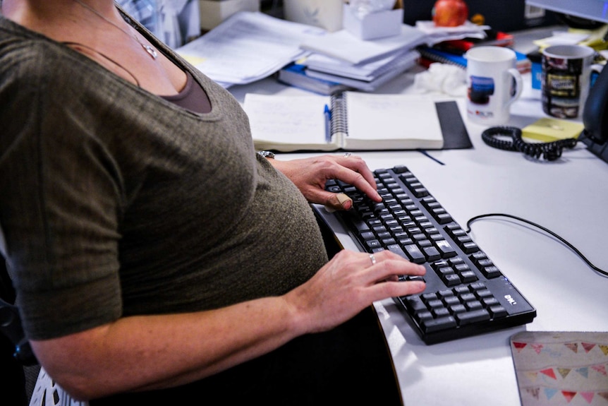 A pregnant woman works at her desk.