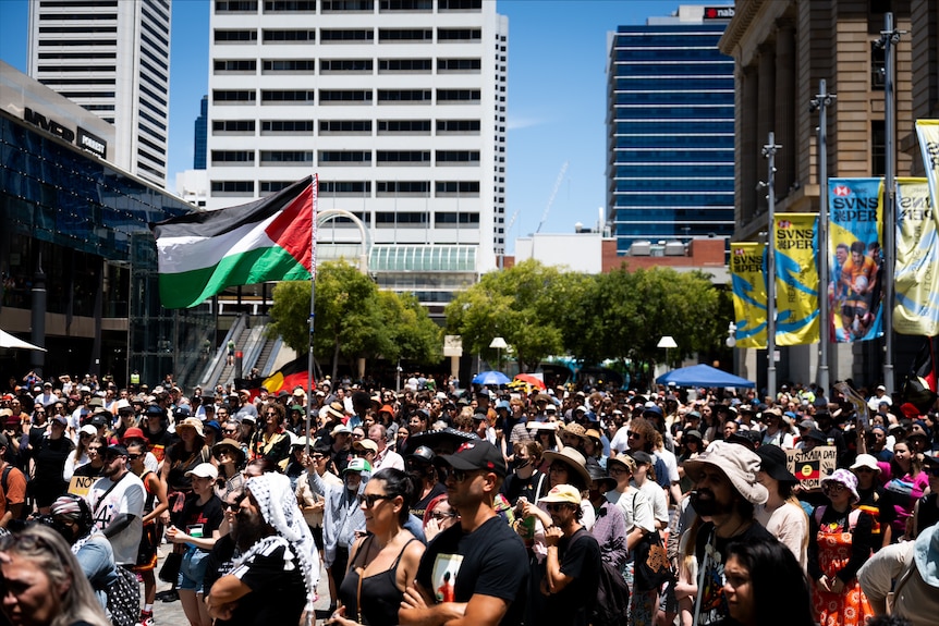 A large crowd of people and both the Palestinian and Aboriginal flags flying.
