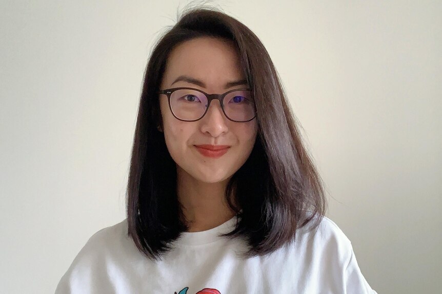 A headshot of a Chinese woman smiling with glasses, white t-shirt and shoulder-length hair. 