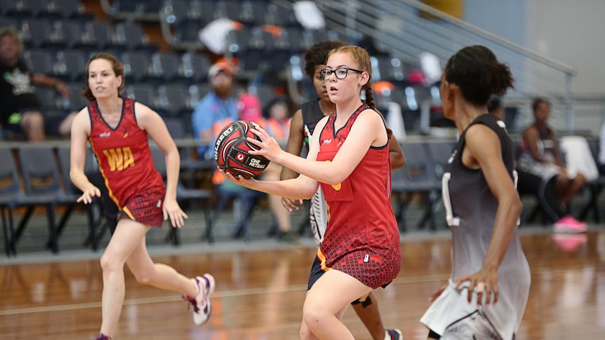 Girls are playing netball on an indoor netball court, and a girl is preparing to pass the netball.