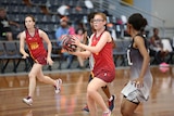 Girls are playing netball on an indoor netball court, and a girl is preparing to pass the netball.
