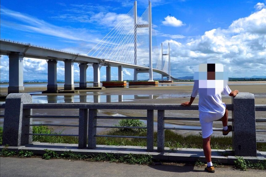 An unidentified Korean businessman stands in front of a bridge. His face has been blurred out.