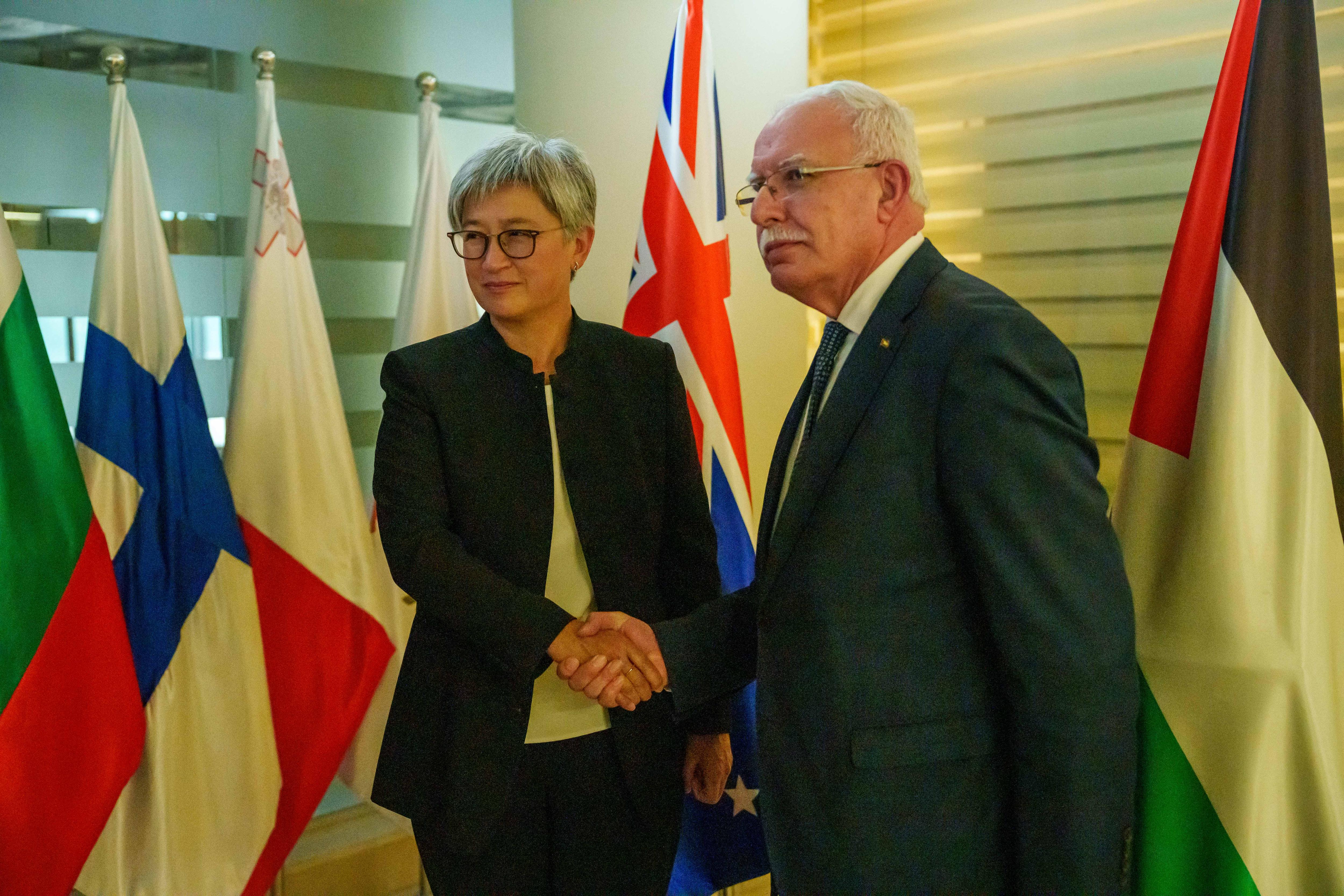 A medium shot of a man and a woman, both in suits and glasses, smiling slightly and shaking hands
