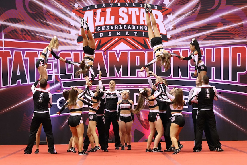 Cheer squad with two cheerleaders flipping in the air, pictured in article about cheerleading and Netflix series Cheer.