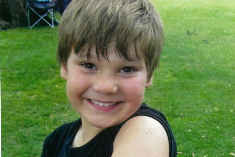 A young boy smiling showing off his left arm with a temporary tattoo of a skull on it
