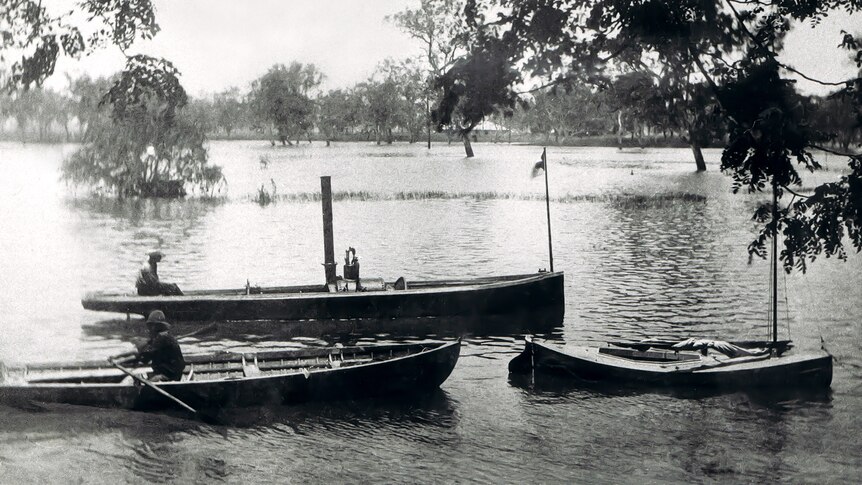 Black and white photo of the steamboat with two other, smaller boats on a flooded creek. 