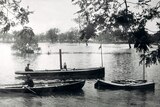 Black and white photo of the steamboat with two other, smaller boats on a flooded creek. 