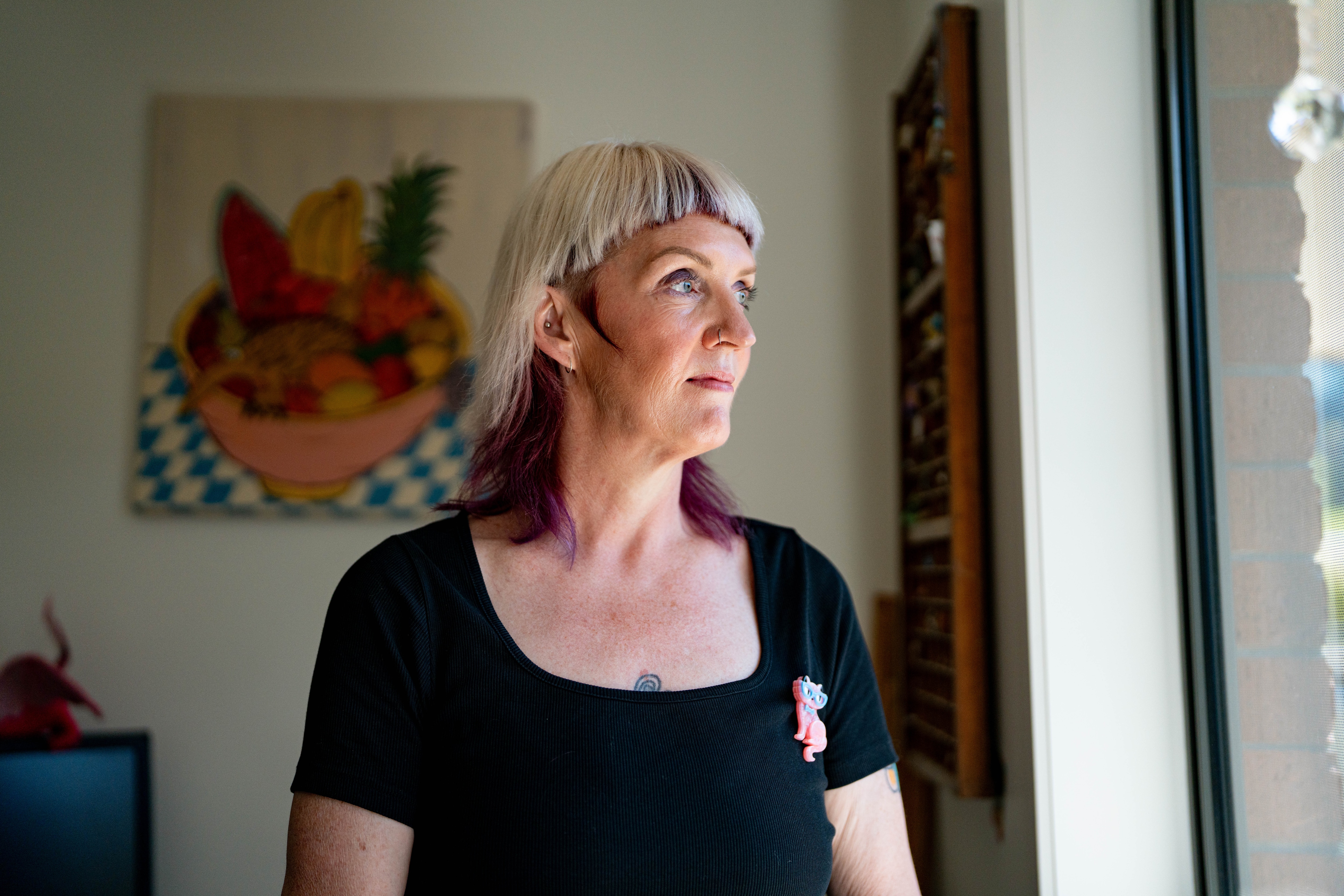 Leonie, wearing a black t-shirt with a pink cat broch, looks out the window in a light-filled office.