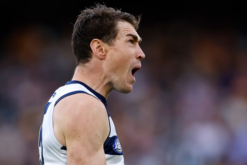 A Geelong AFL player screams out as he celebrates kicking a goal.