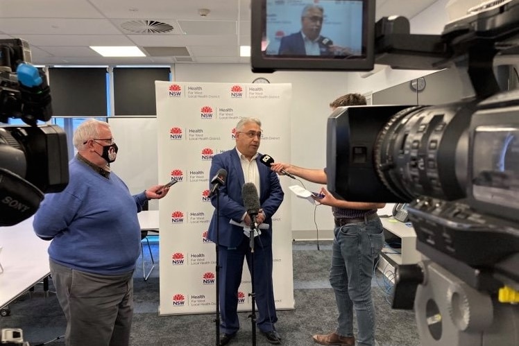 A man with a blue suit speaking to reporters in front of cameras. 