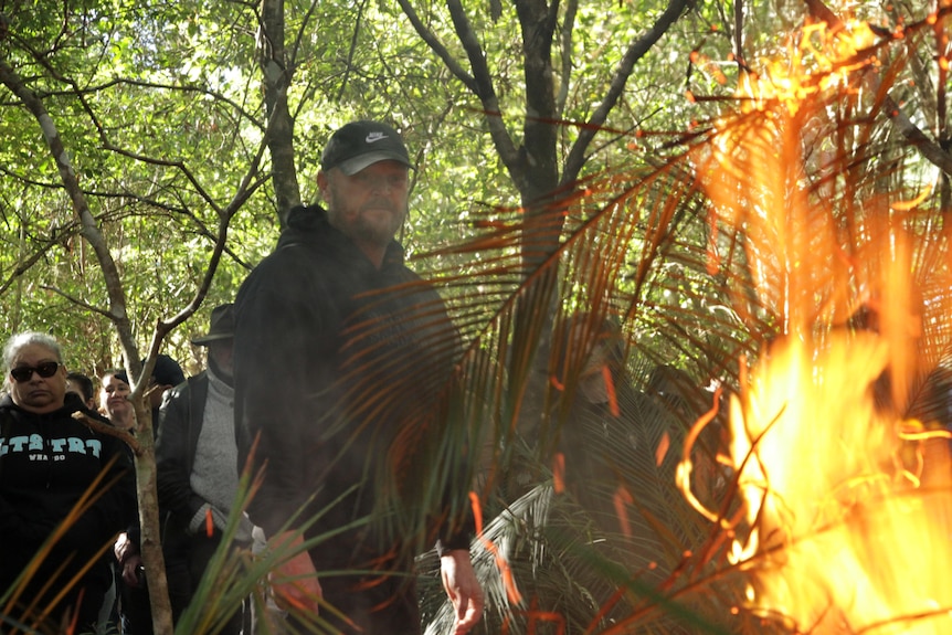 A man looks into a fire in bushland.