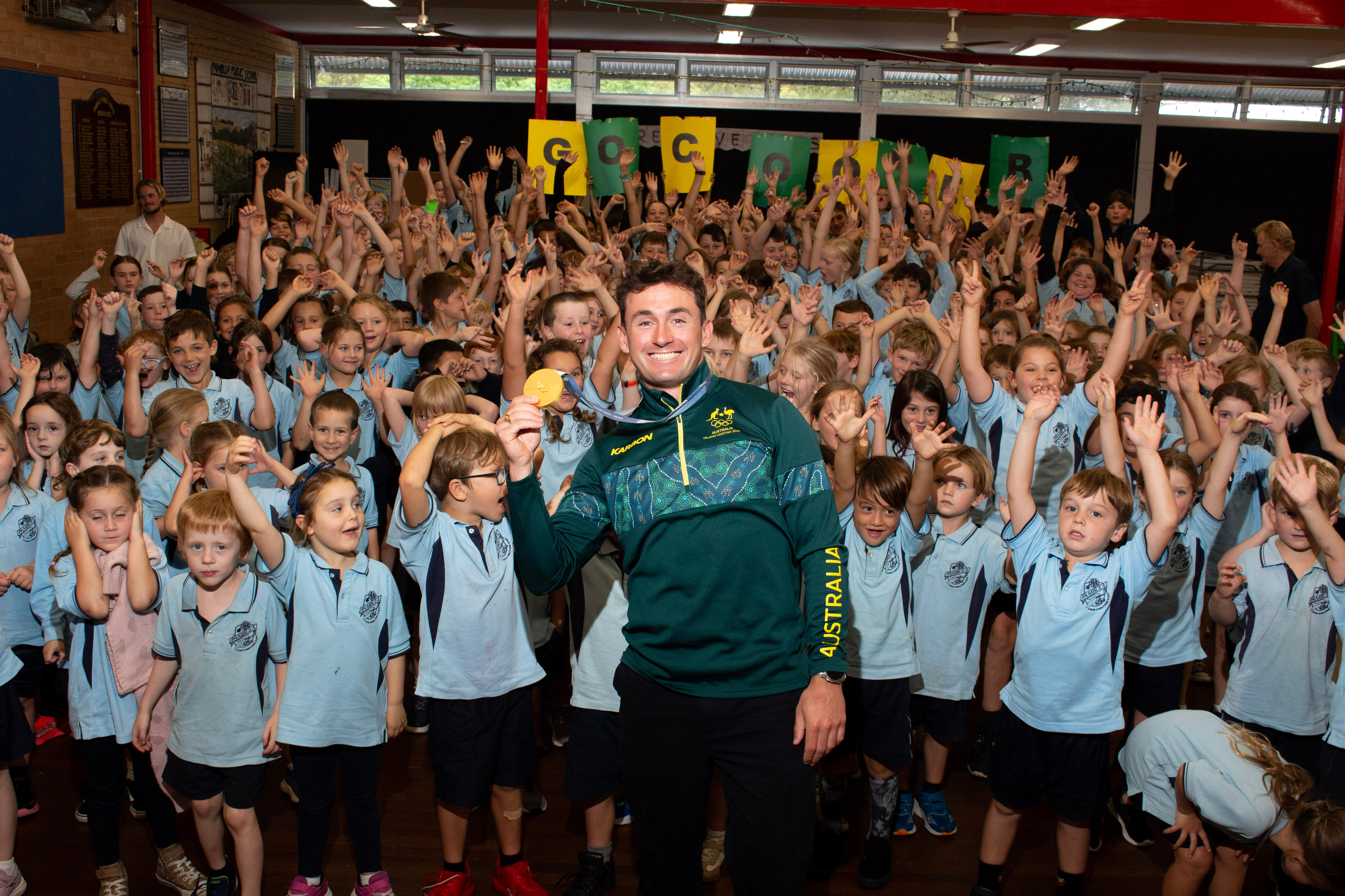 a man holds a gold medal with kids cheering