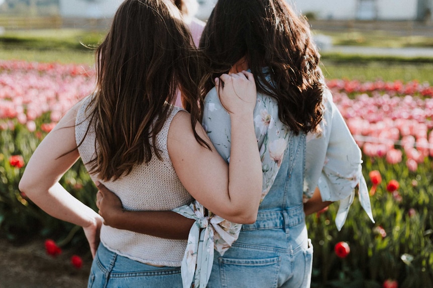 Two women face a garden with arms around each other