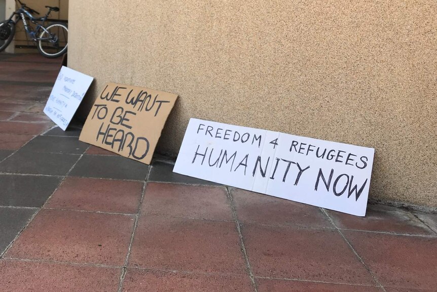 Photograph of three protest signs leaning against a wall.