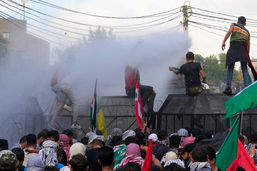 Riot police spray protesters, some who have scaled a security fence, with a water cannon during a demonstration.