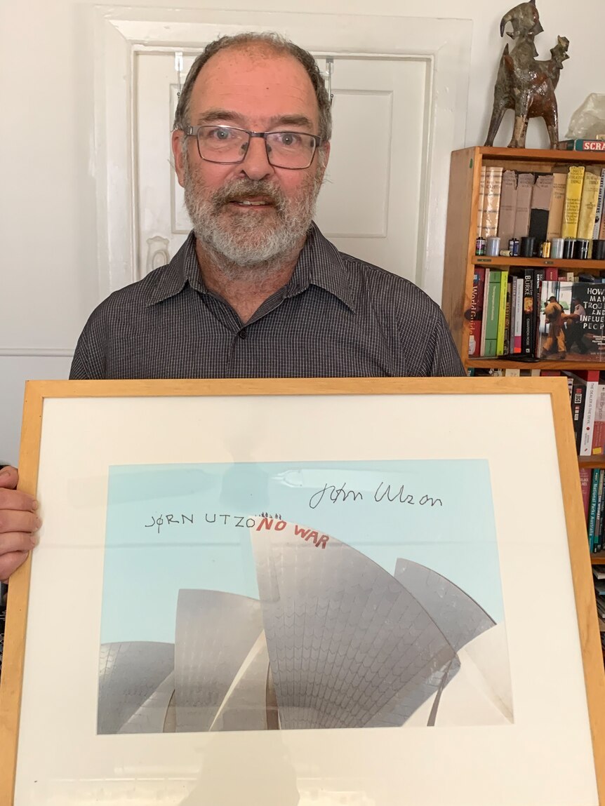 Man with glasses holding a framed picture of the Sydney Opera House. 