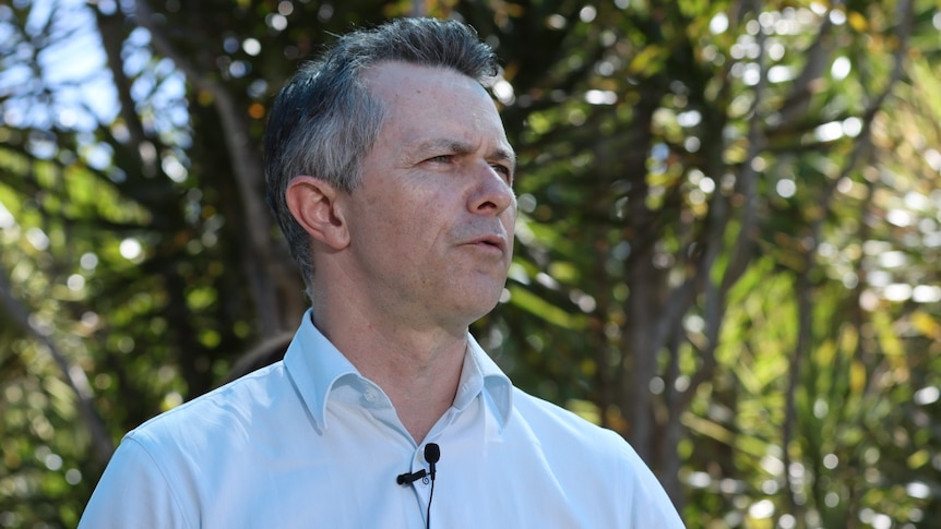 Jason Clare wearing a blue business shirt and looking with interest to his left. 