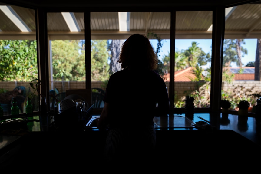 A silhouette of a woman standing in a kitchen with a bay window.