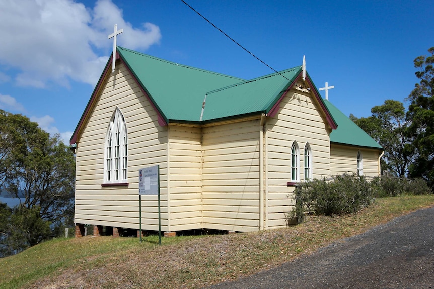 The side of a small cream church with a green roof.