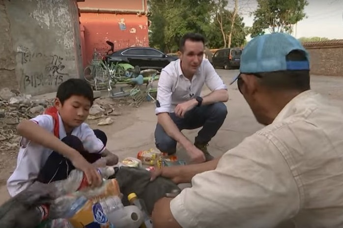 Birtles crouching talking to Wang Jindong as his nephew puts bottles in a bag.
