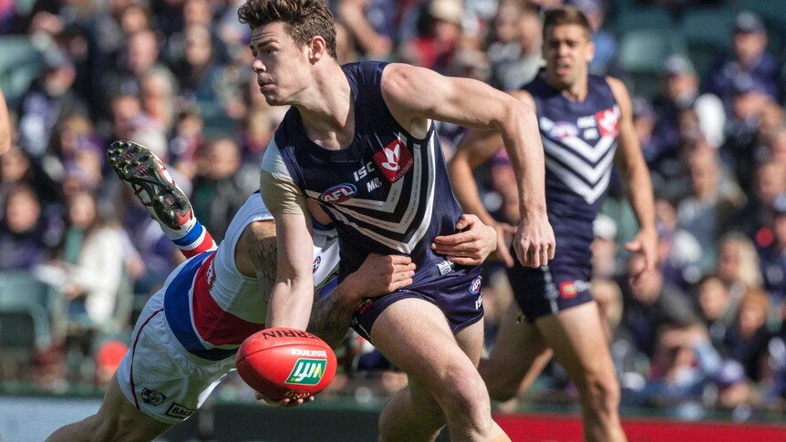 Lachie Neale handballs a football while being tackled by a Western Bulldogs player.