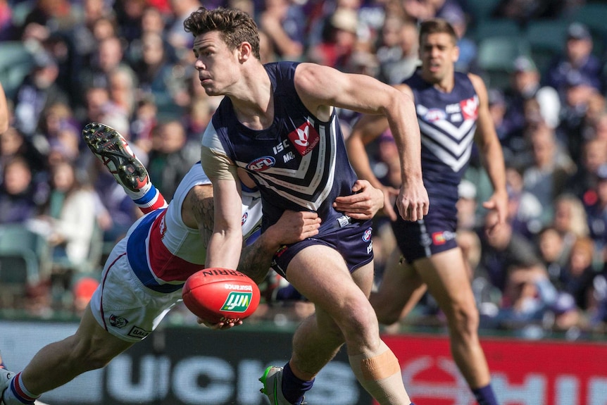 Lachie Neale handballs a football while being tackled by a Western Bulldogs player.