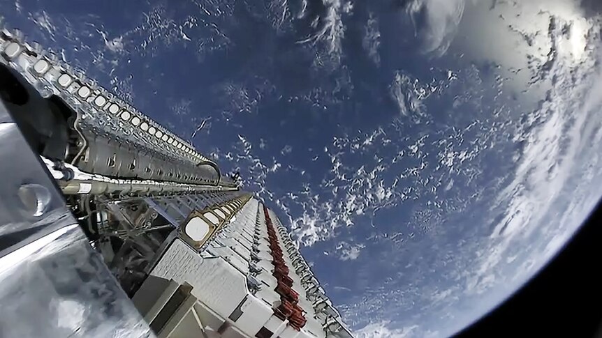 A camera on board a satellite looks down towards Earth showing part of the satellite and the planet.
